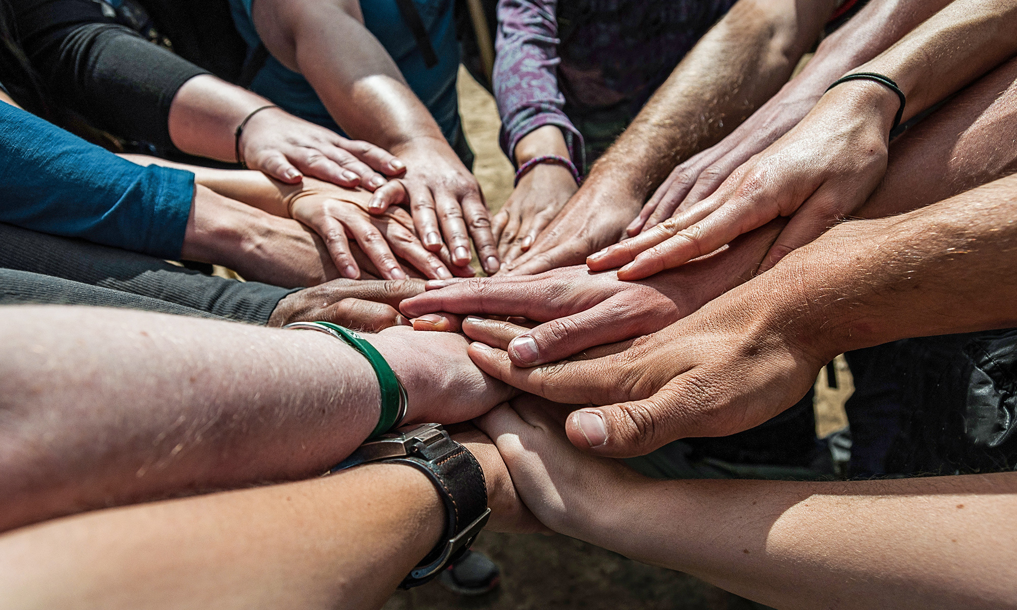 Stack of hands of men and women outside in the sun