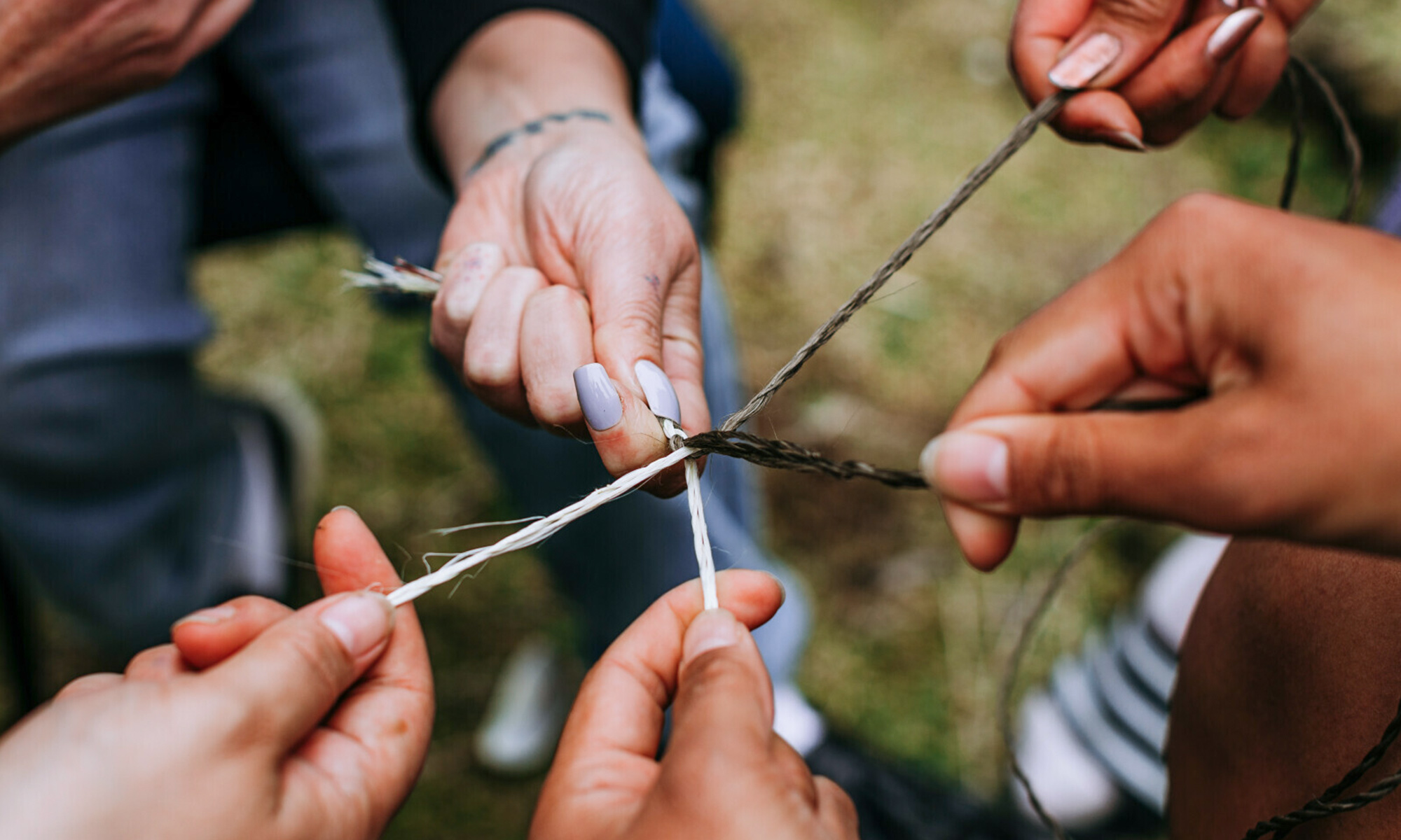 Five different people intertwining and weaving string together